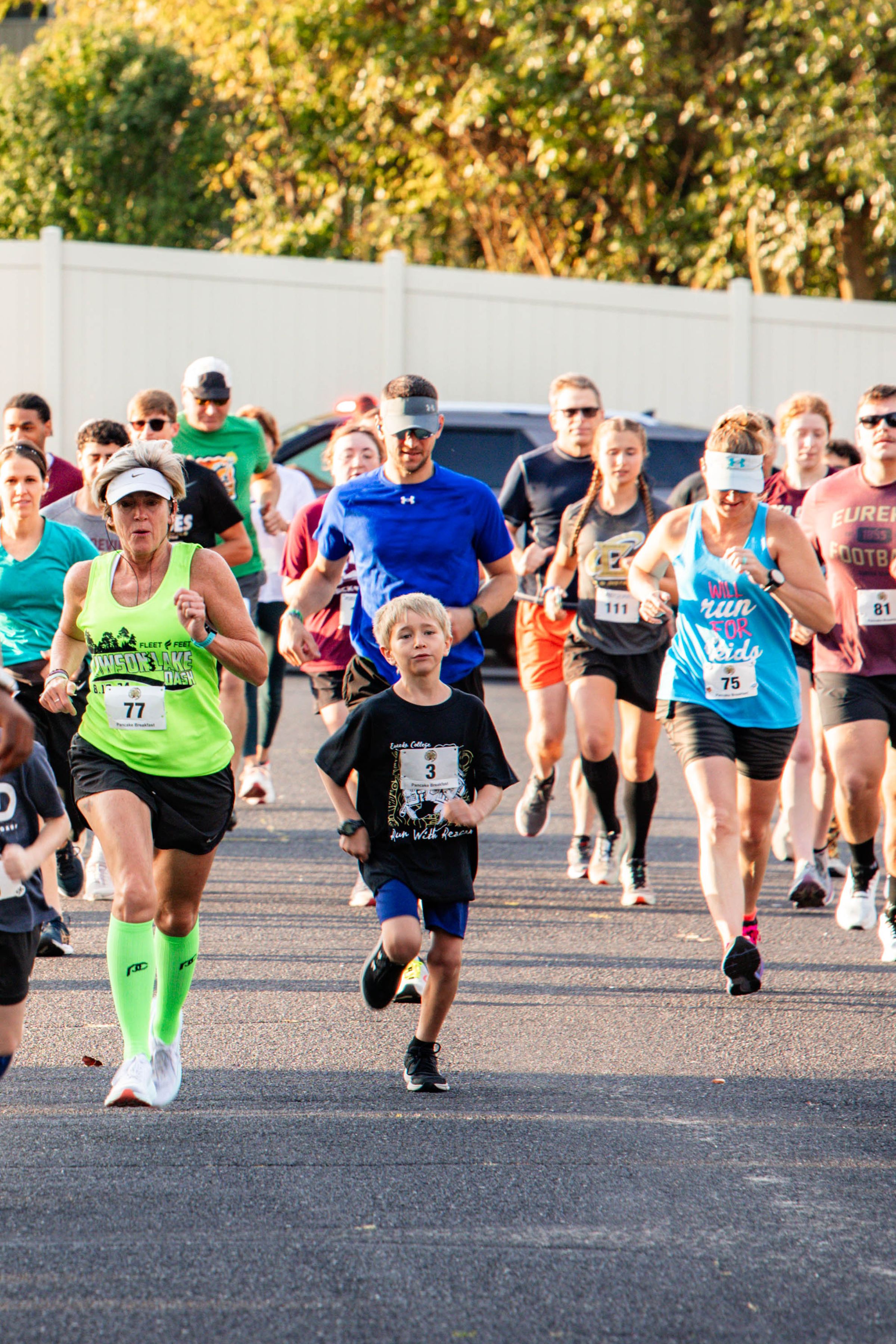 A pack of runners wearing race bibs on the road during Run with Reagan