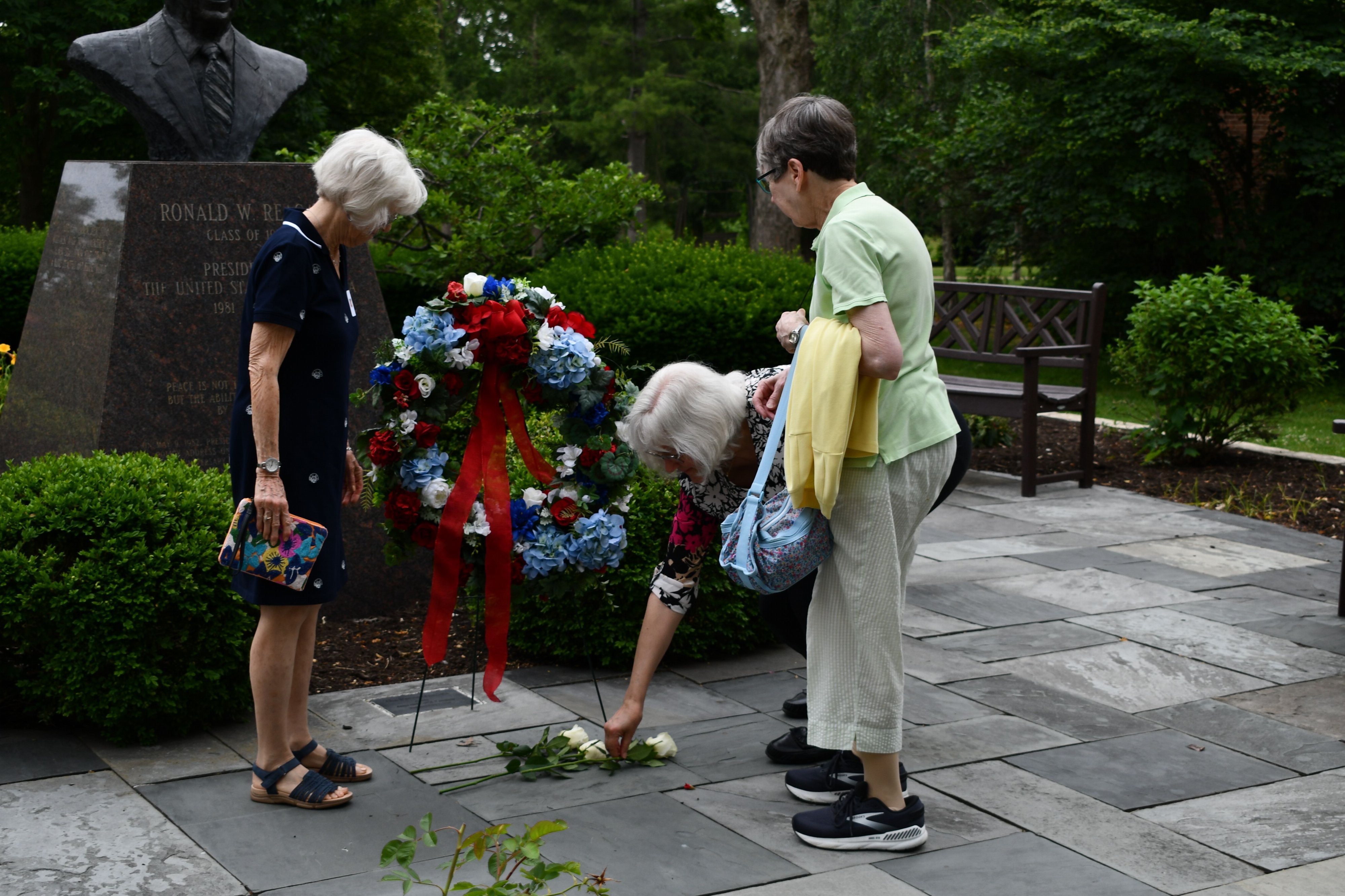 Three visitors lay white roses on the pavement beside a red, white and blue wreath at the bronze bust of Ronald W. Reagan in the Eureka College Peace Garden